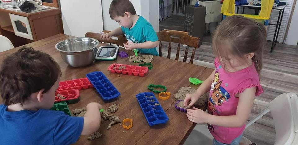 Three children playing with dough and ice cube trays at a table