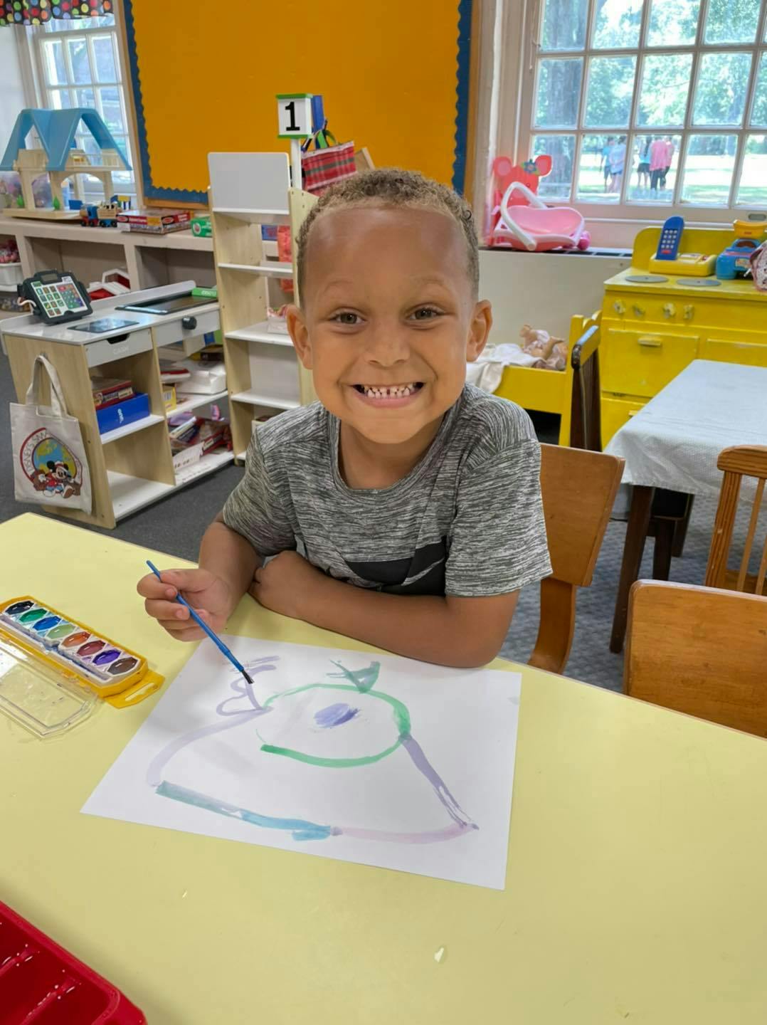 Child painting a picture at a table in a classroom