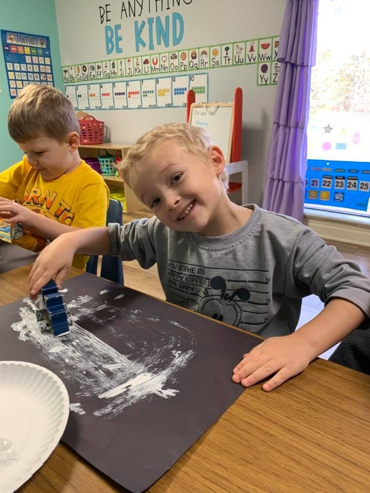 Child making art with white paint on black paper