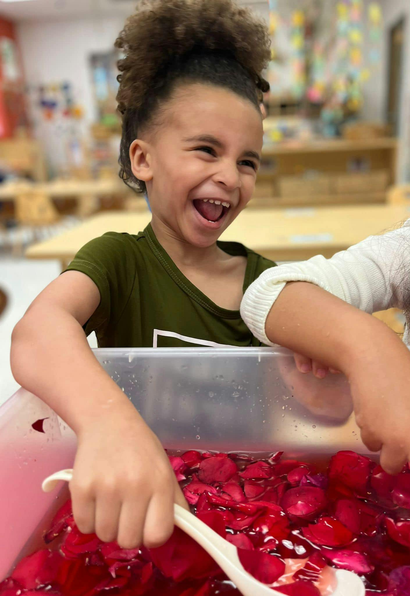 Child playing with red petals in water with a spoon