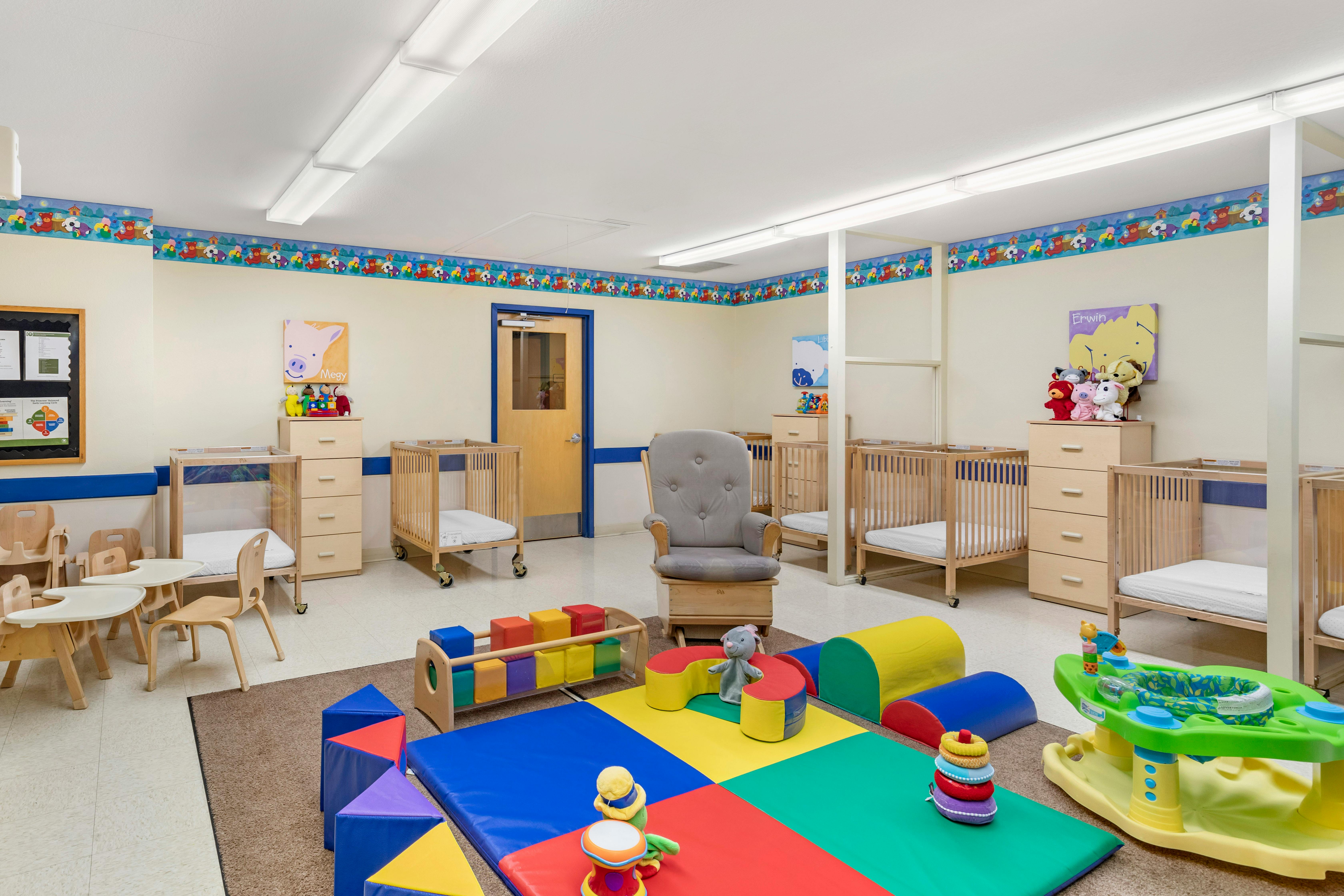 Baby room with cribs, play mats, child-sized tables and chairs, and a rocking chair
