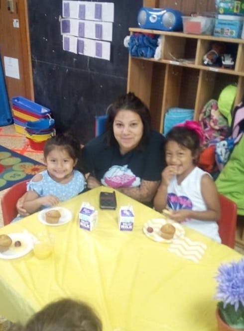 Person and two children sitting at a table with food and drinks