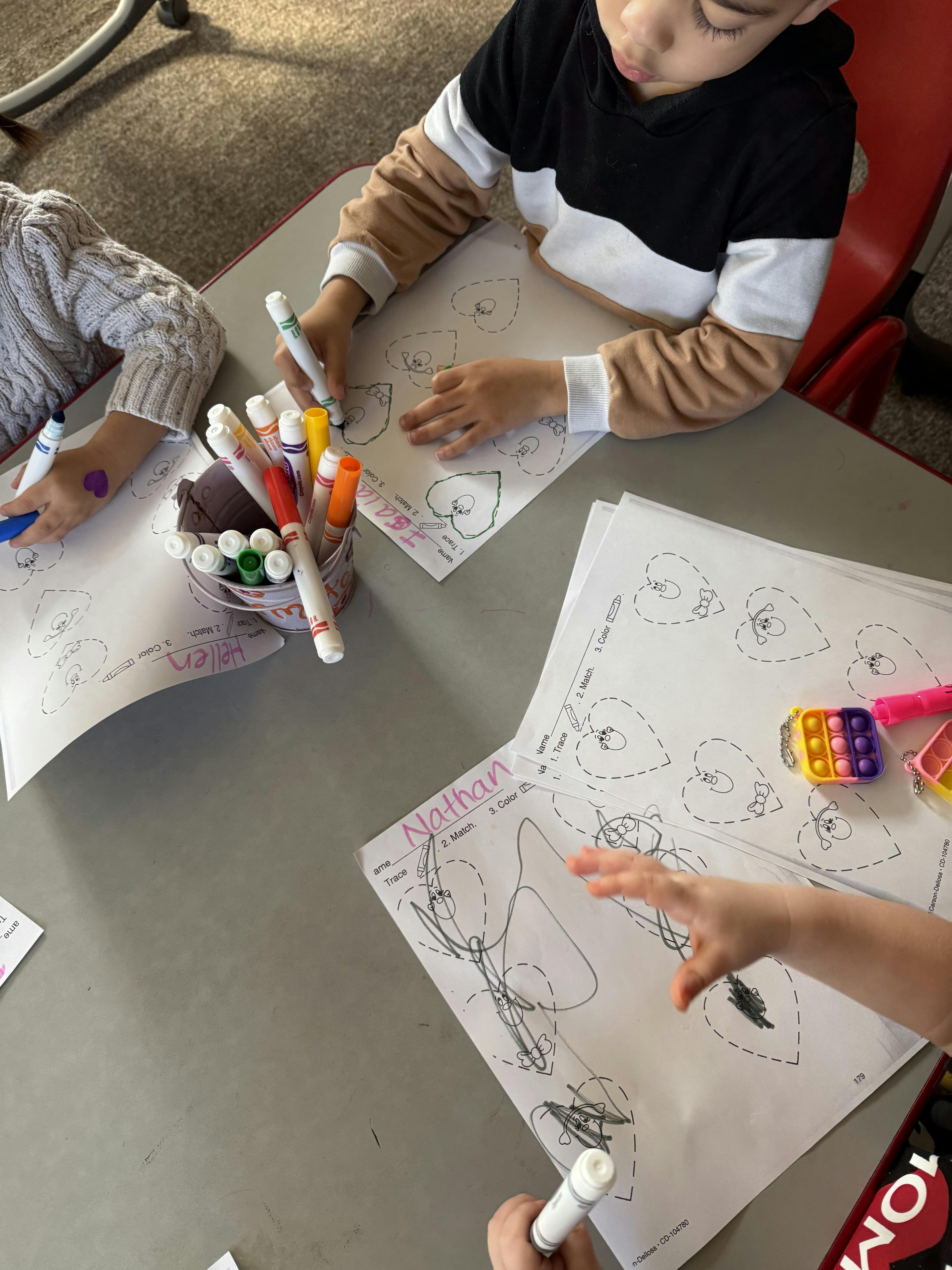 Children coloring worksheets at a table with markers