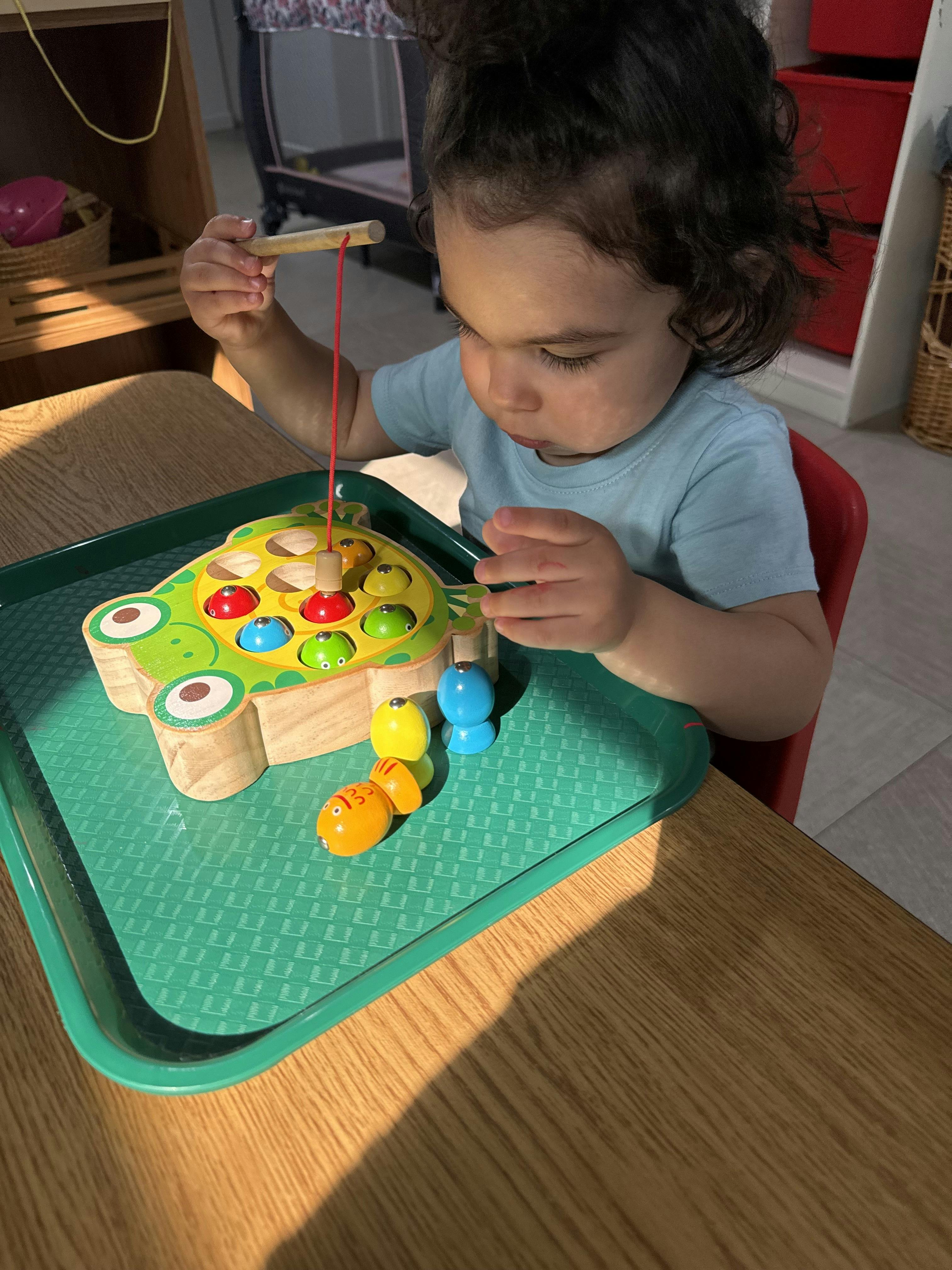 Child playing with a wooden magnetic fishing toy on a green tray