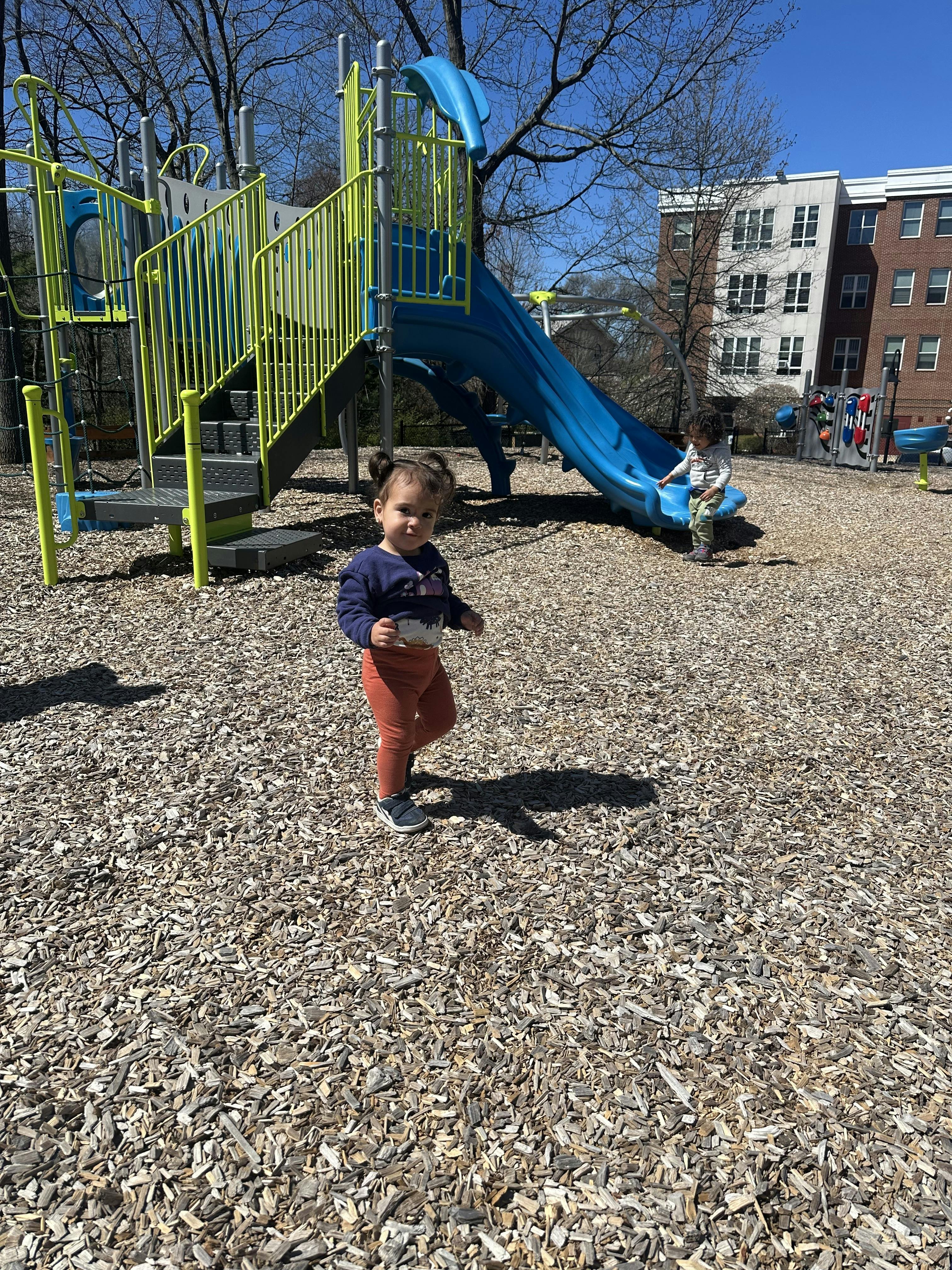 Child standing on wood chips in front of a blue and yellow playground