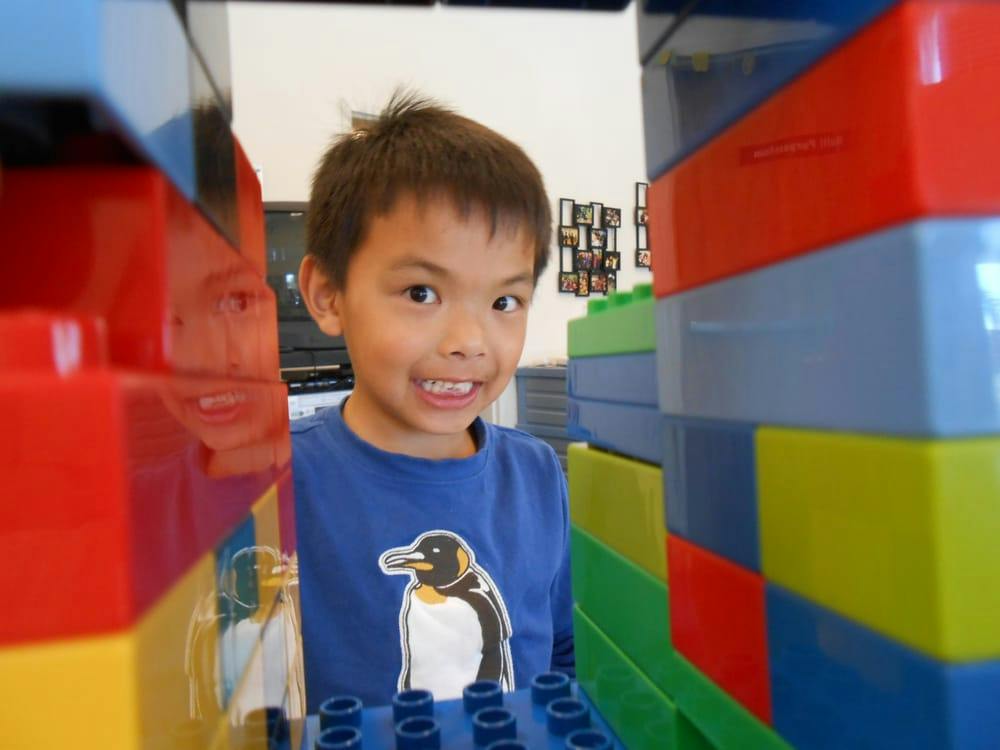 Child in a blue shirt with a penguin on it, peeking through colorful blocks