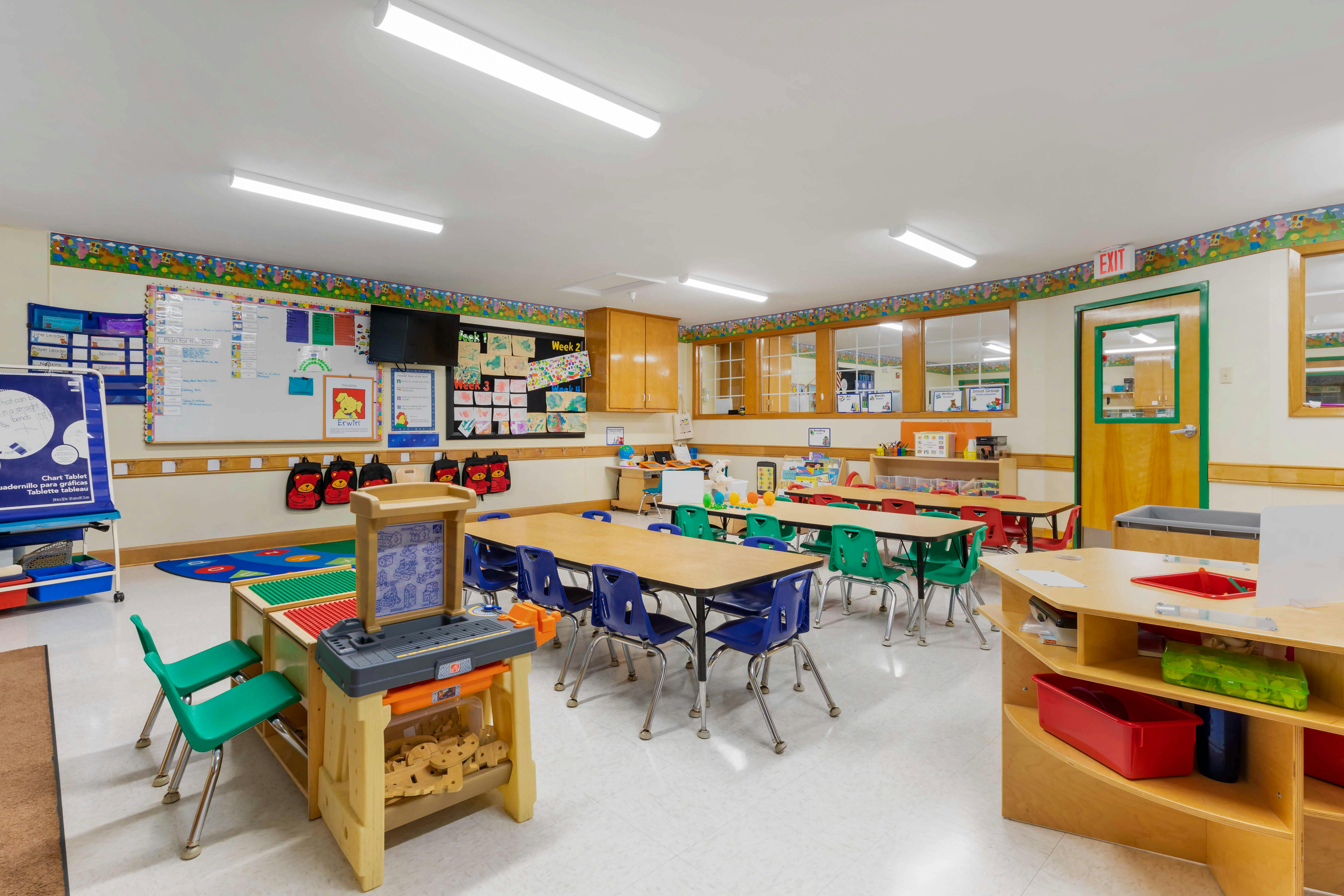Classroom with tables and chairs, a whiteboard with "Plan for the Day" and artwork