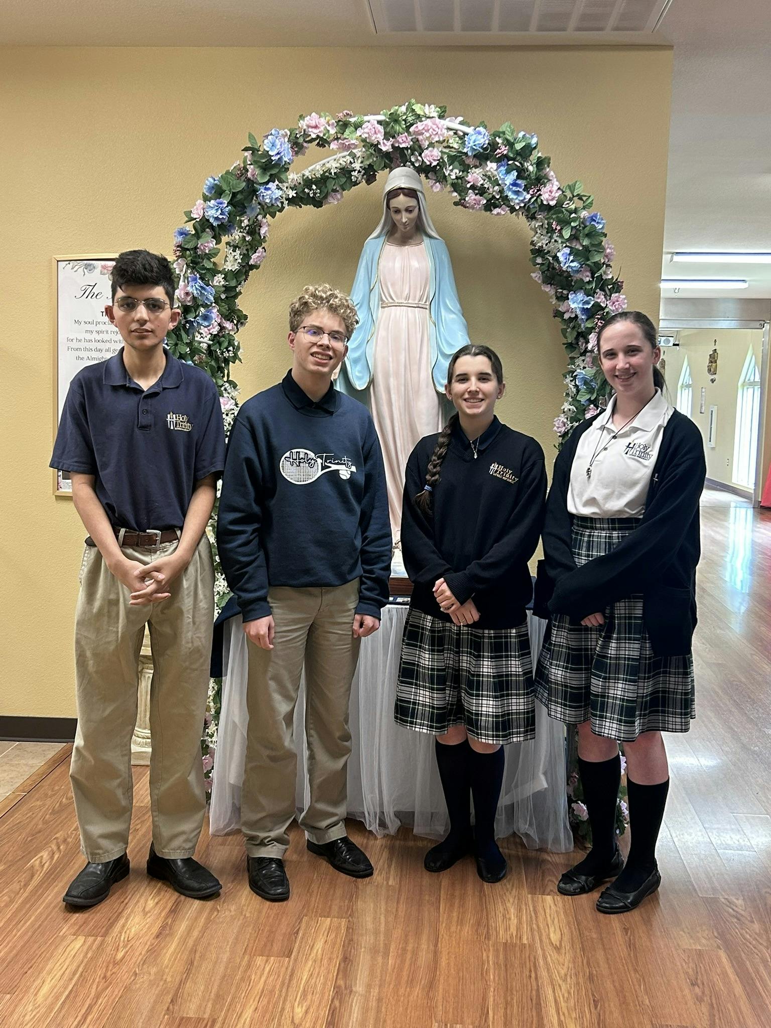 Four teens in school uniforms standing in front of a statue of Mary