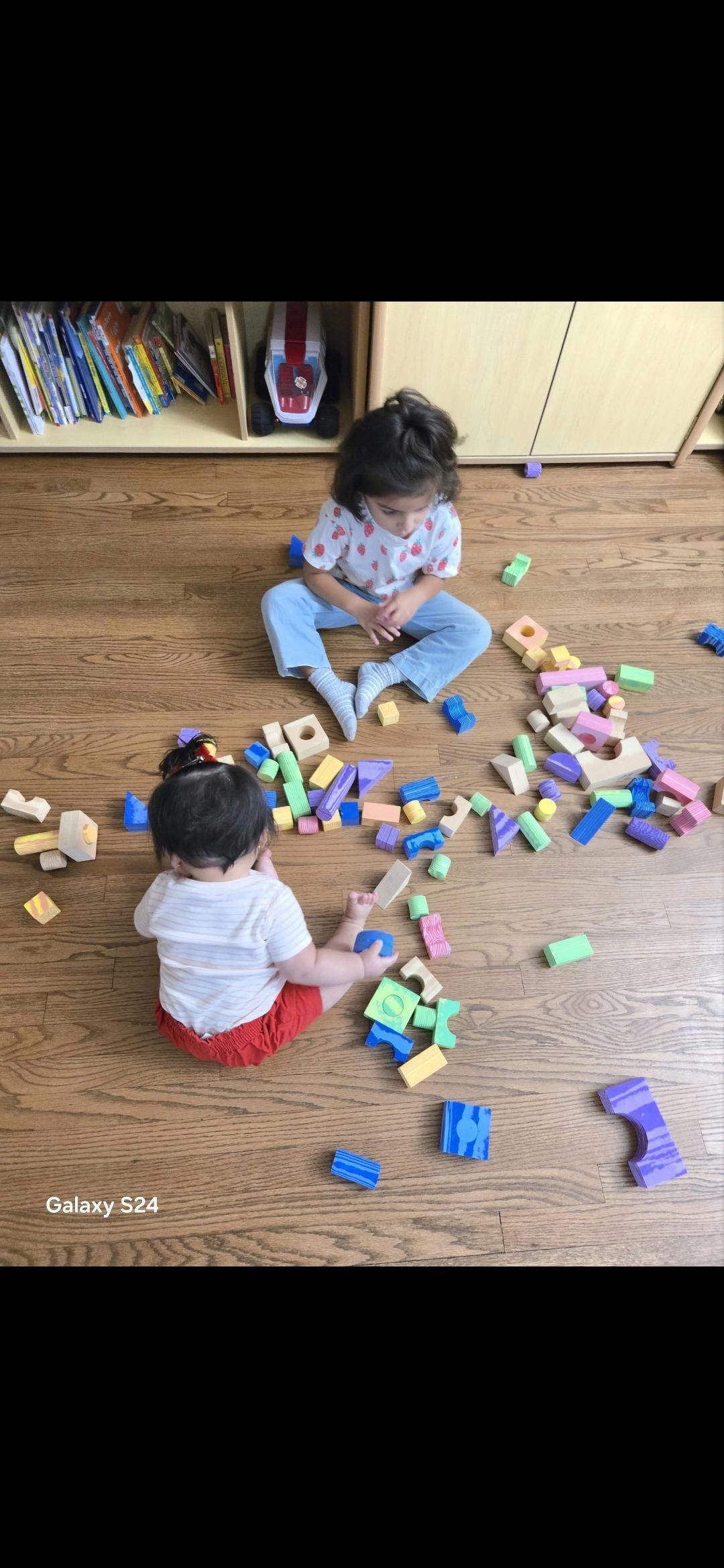 Two children sitting on the floor playing with colorful wooden building blocks