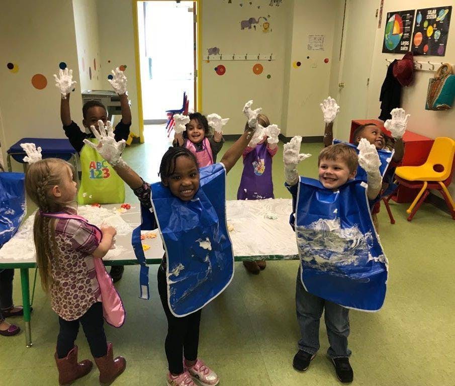 Children in aprons and gloves raising hands in a classroom