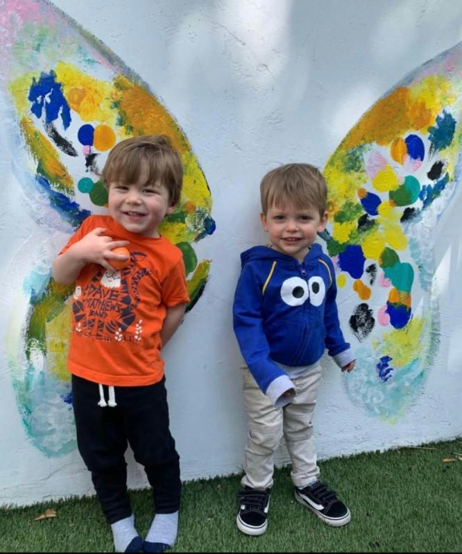 Two children standing in front of a painted butterfly wing mural