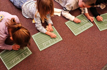 Children lying on floor writing on small chalkboards