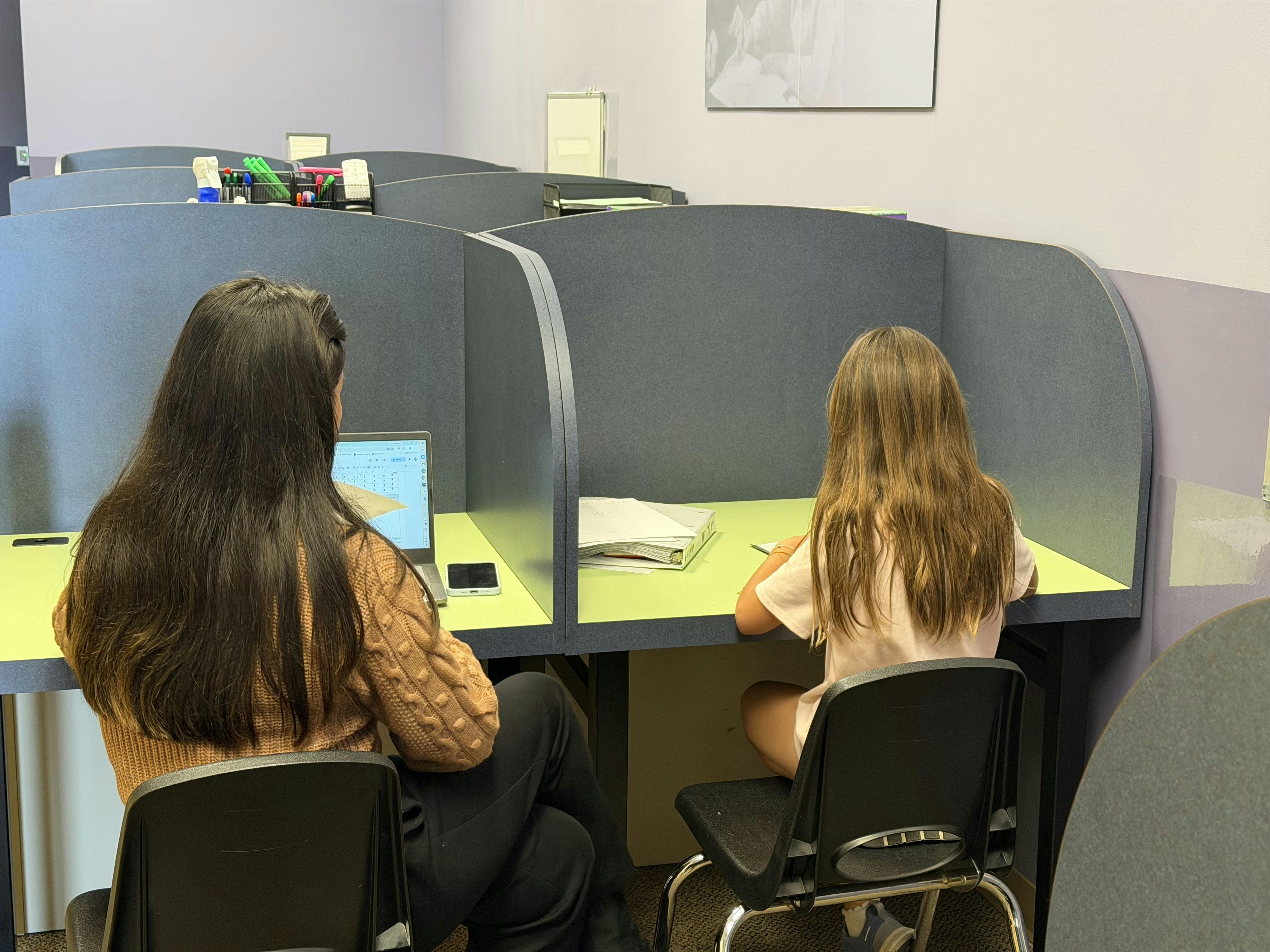 A person and a child working at separate partitioned desks