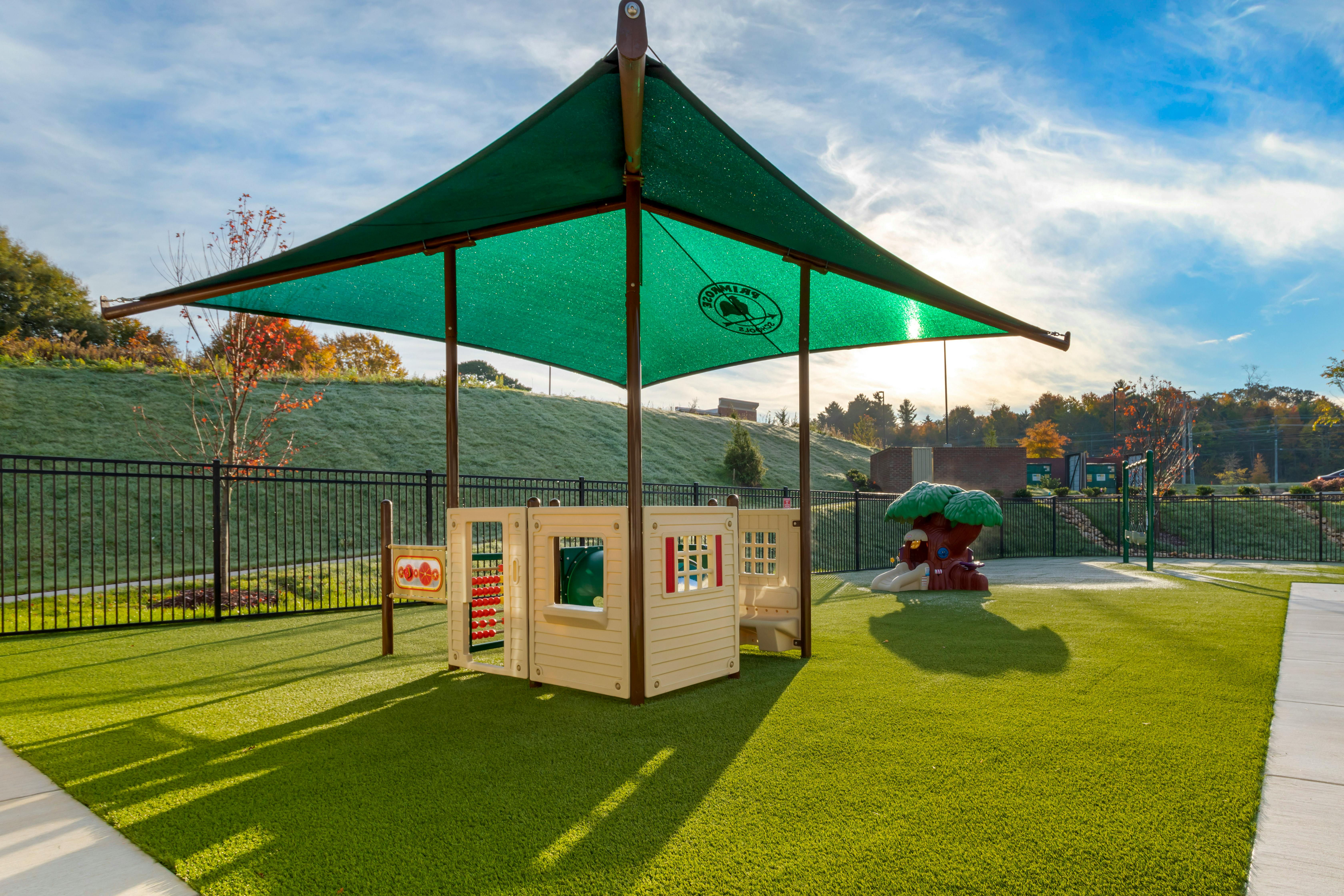 Playground with green shade structure, playhouse, and tree-shaped slide