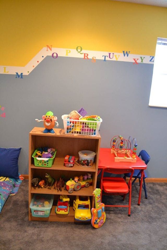 Playroom with toy shelf, small red table and chairs, and alphabet letters on wall