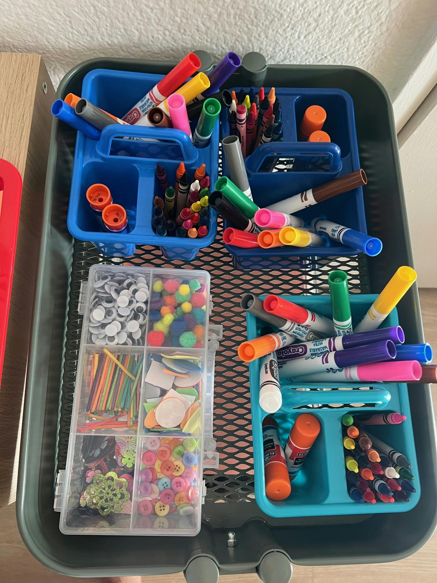 Art supplies including markers, crayons, googly eyes, and pom-poms in organizers