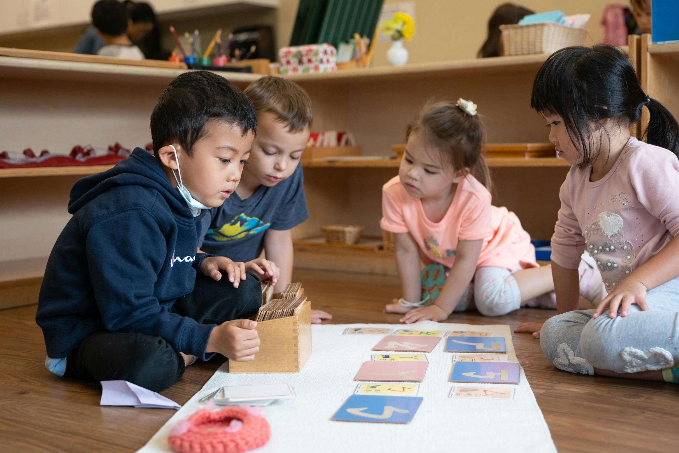Four children playing with cards and blocks on the floor in a classroom