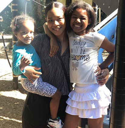 Person holding a child and standing next to another child on a playground
