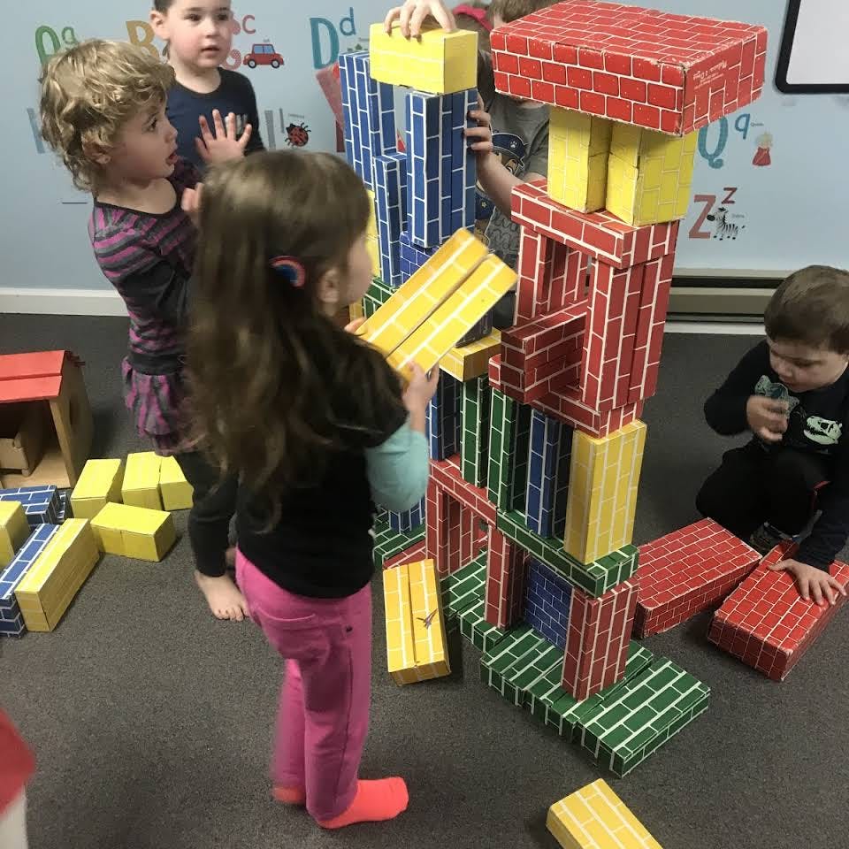 Children building a tall structure with large colorful blocks in a classroom