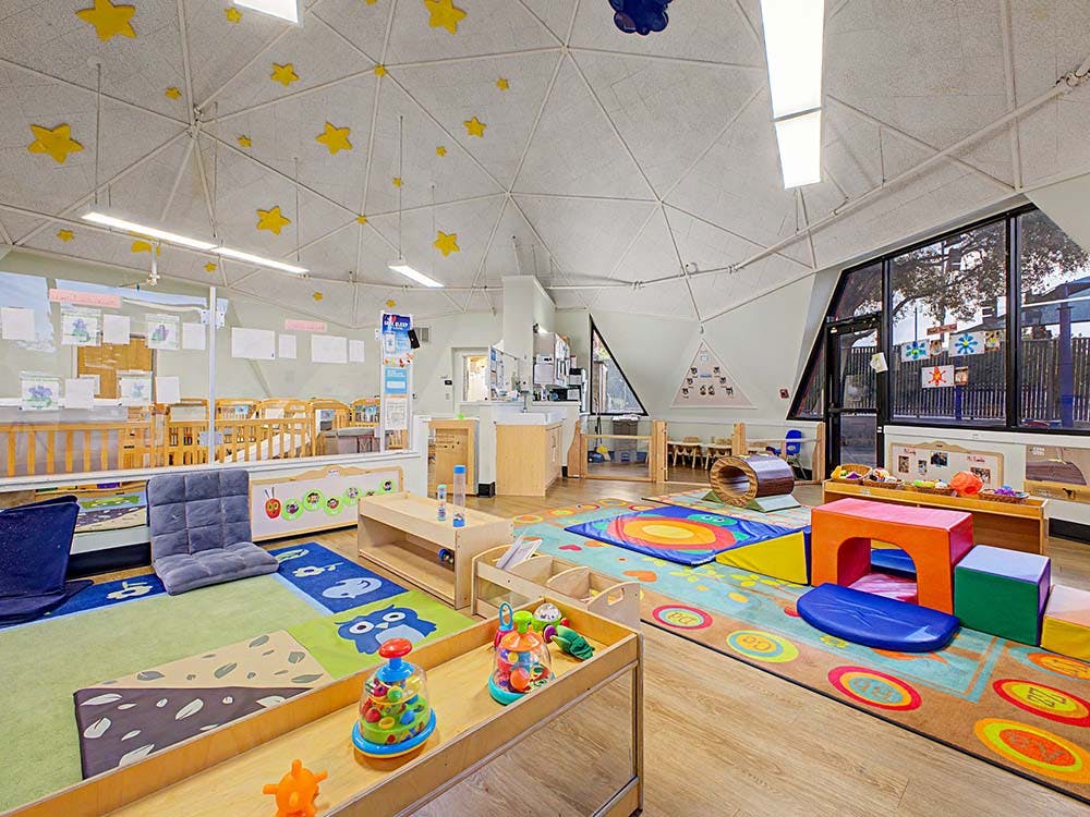 A childcare classroom with cribs, play mats, and learning toys
