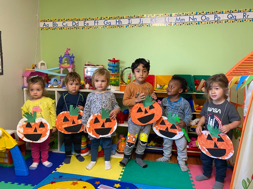 Children in a classroom holding paper plate pumpkin crafts