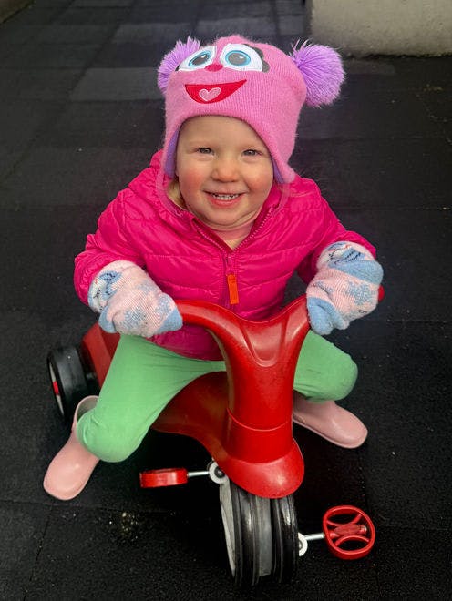 Child in a pink hat and jacket riding a red tricycle