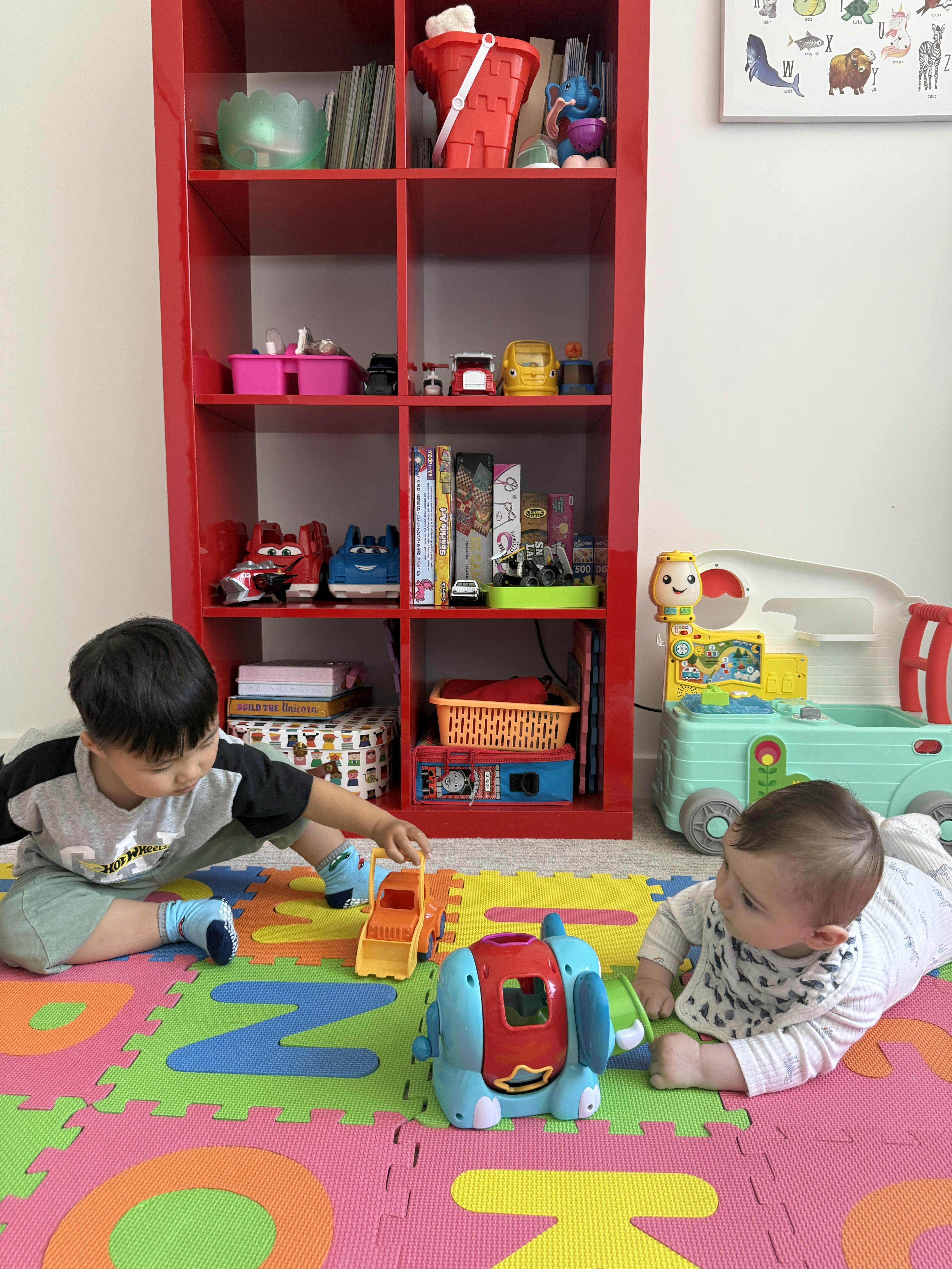 Child playing with a toy truck and baby on a colorful playmat