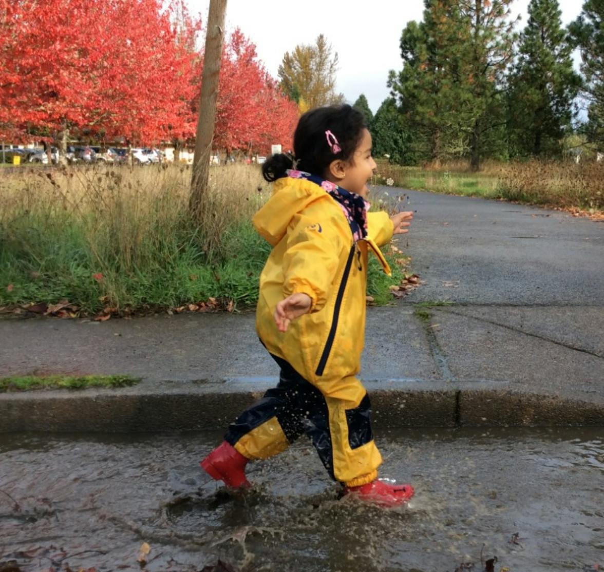 Child in yellow rain suit and red boots splashing in a puddle