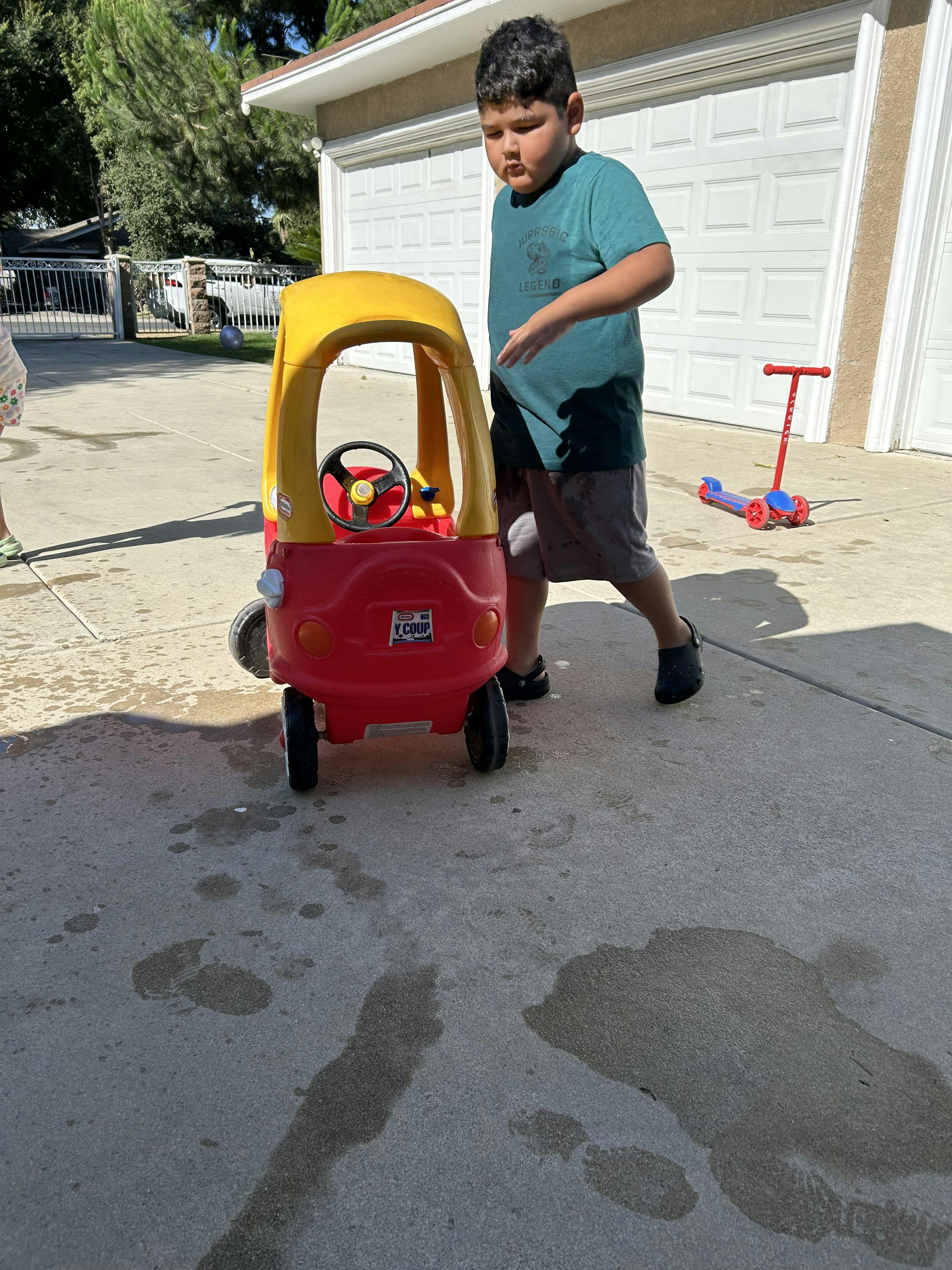 Child standing next to a toy car on a driveway