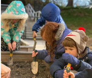 Three children digging in dirt with small shovels