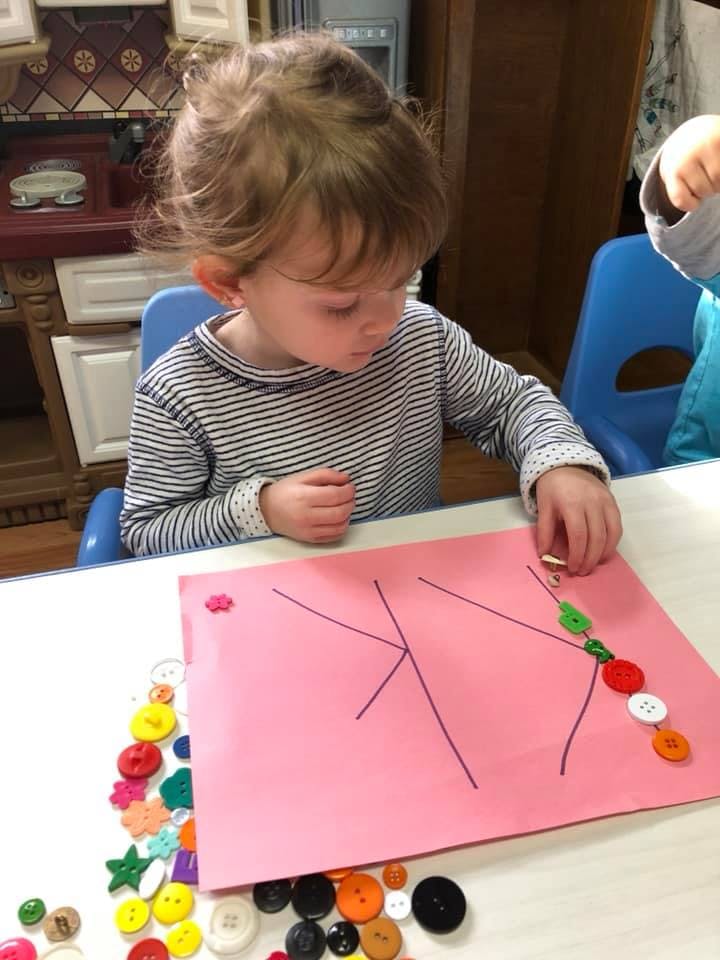 Child placing buttons on a pink paper with drawn lines