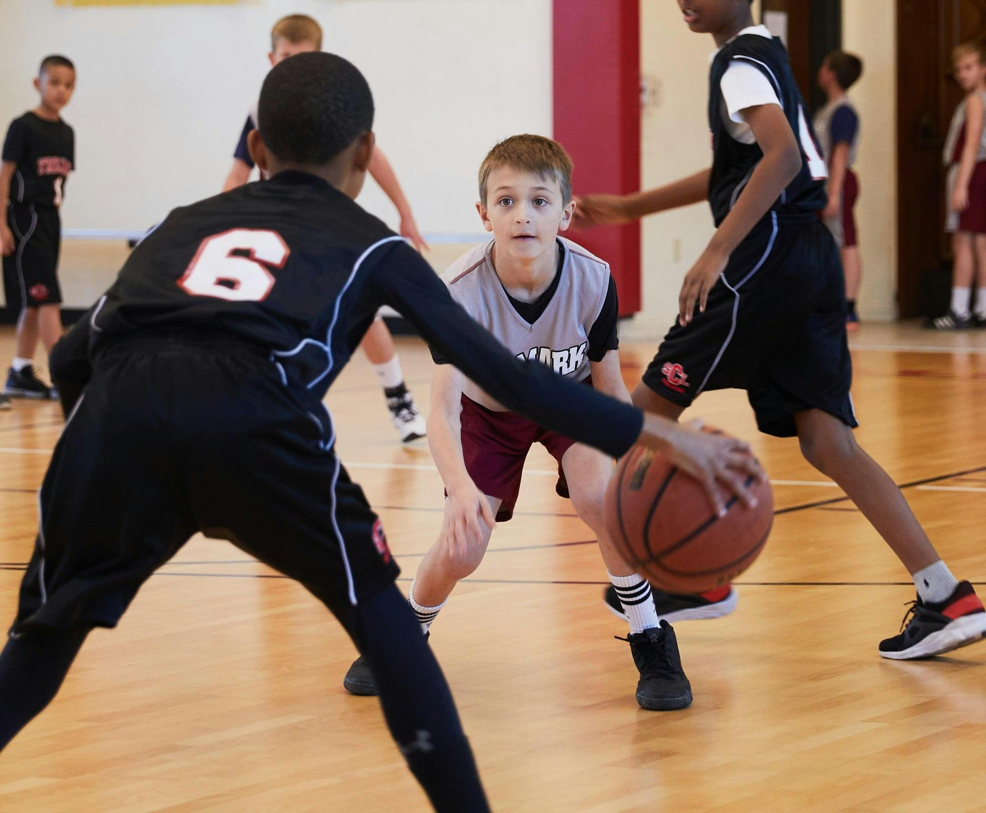 Child in black jersey dribbling a basketball past another child