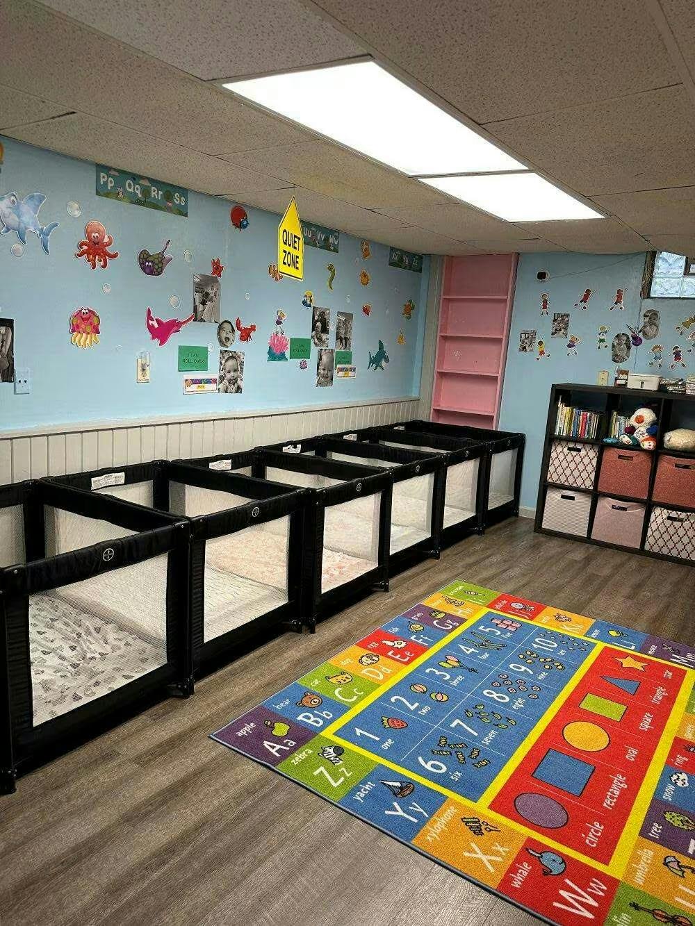 Cribs lined up in a daycare room with an educational alphabet and number rug