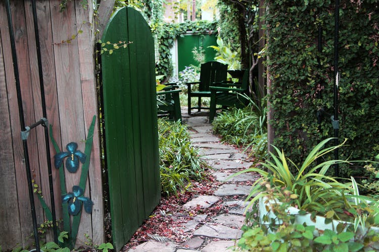 Open green garden gate leading to a stone path and outdoor seating