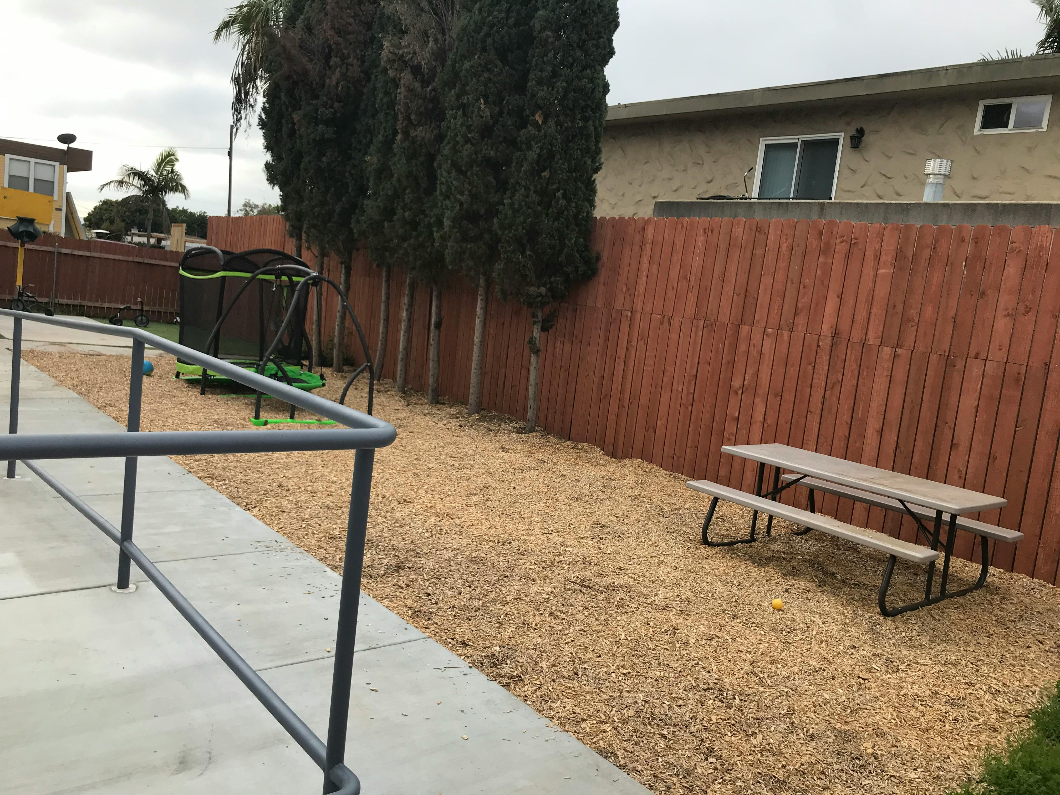 Outdoor area with a picnic table, wooden fence, and a trampoline