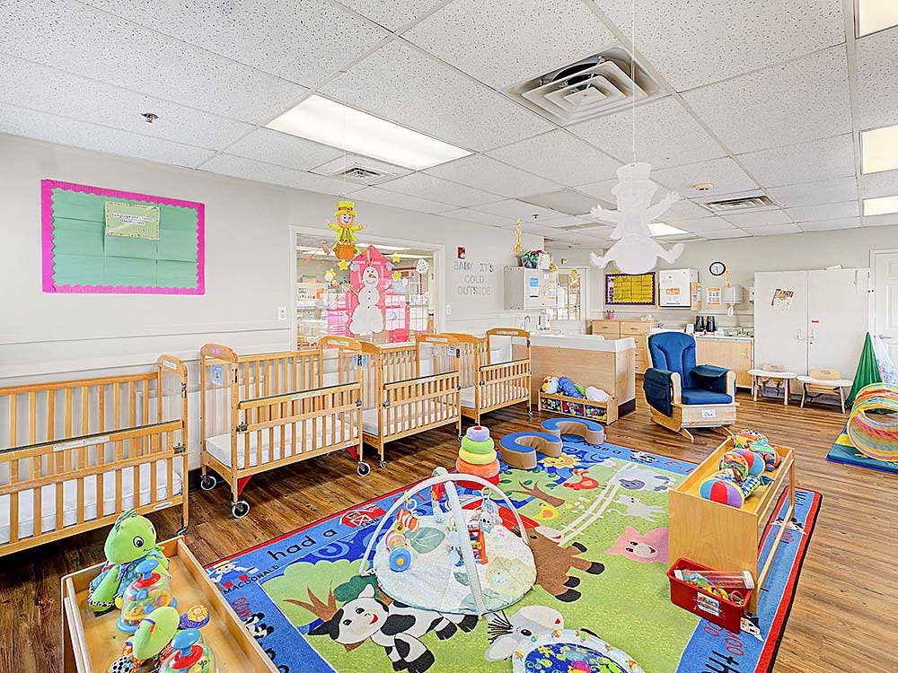 Cribs, a changing station, and colorful toys on a rug in a daycare room