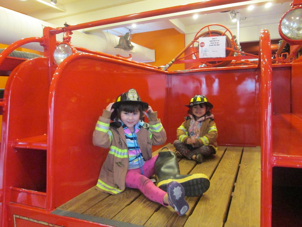 Two children in firefighter costumes sitting in a red fire truck