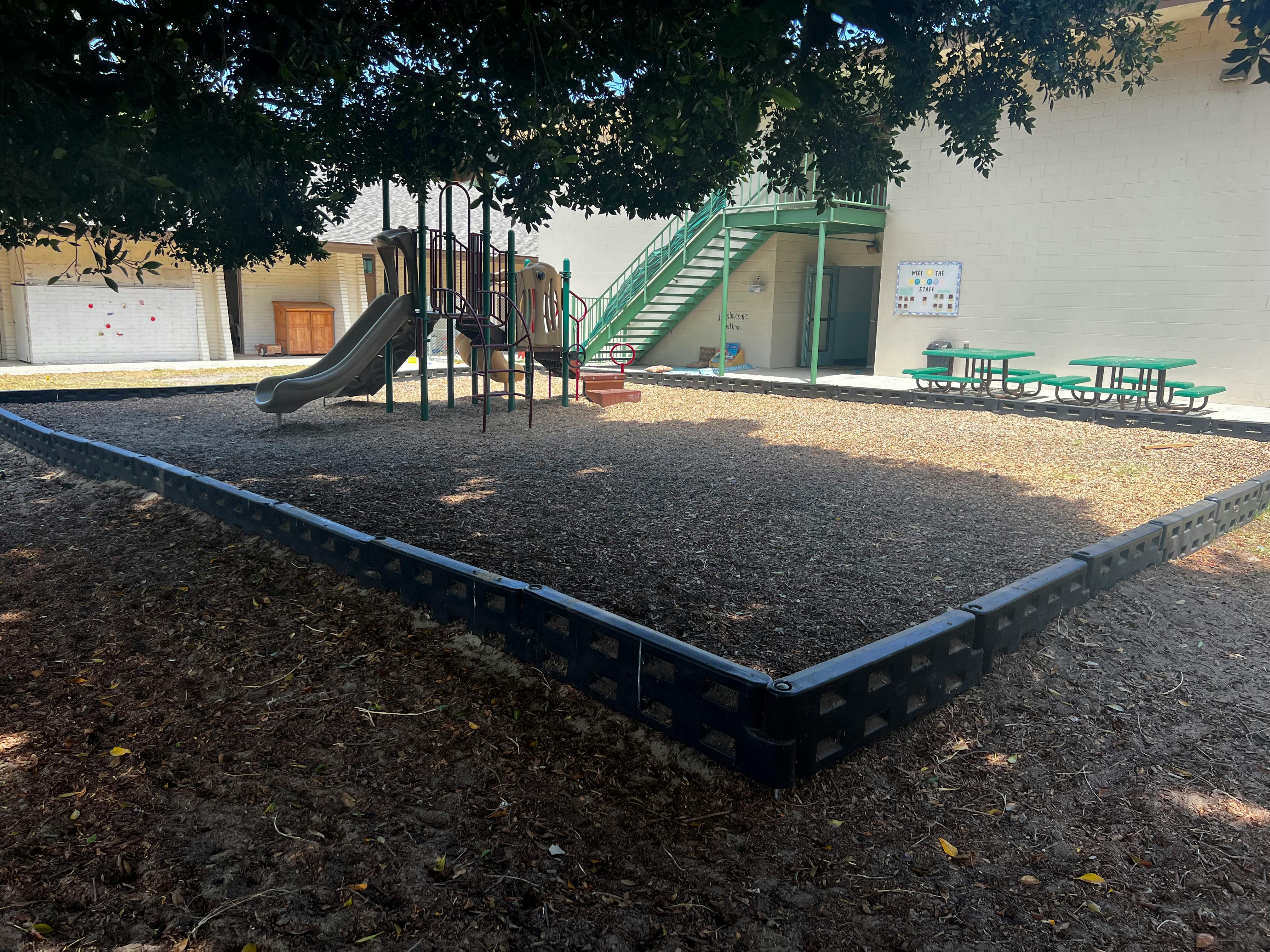 Playground with wood chips, slide, and green picnic tables