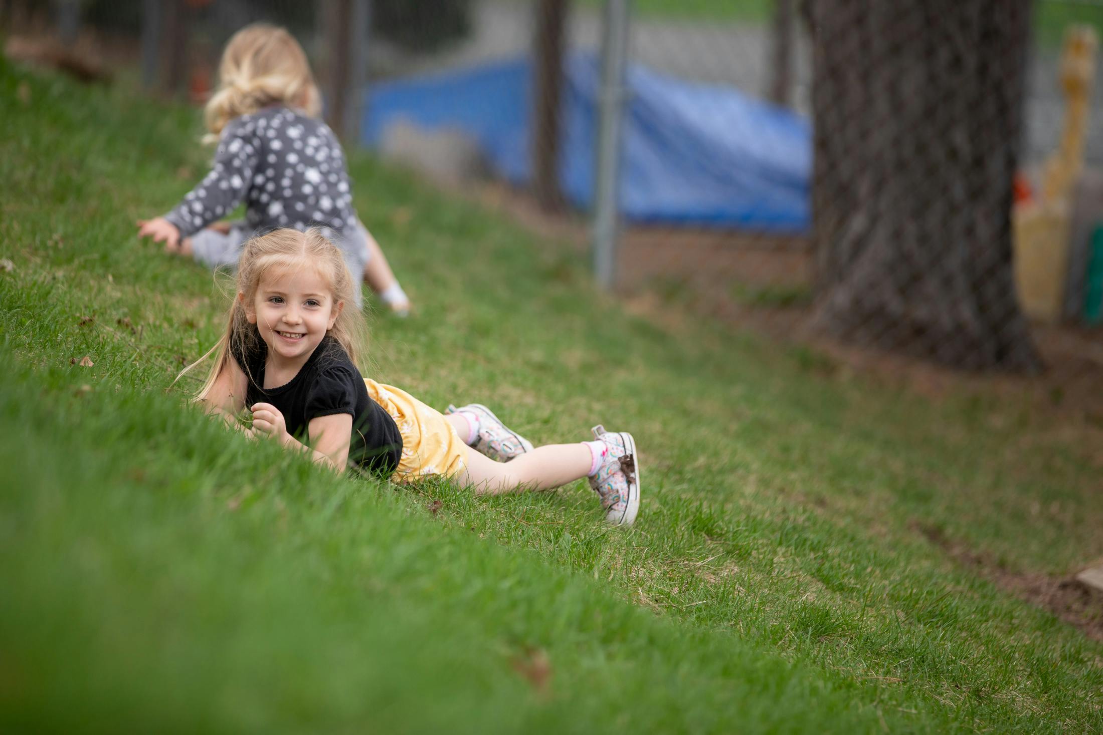 Child lying on a grassy hill, another child in the background