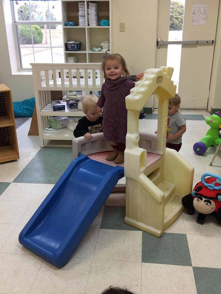 Three children playing on a small slide and play structure indoors