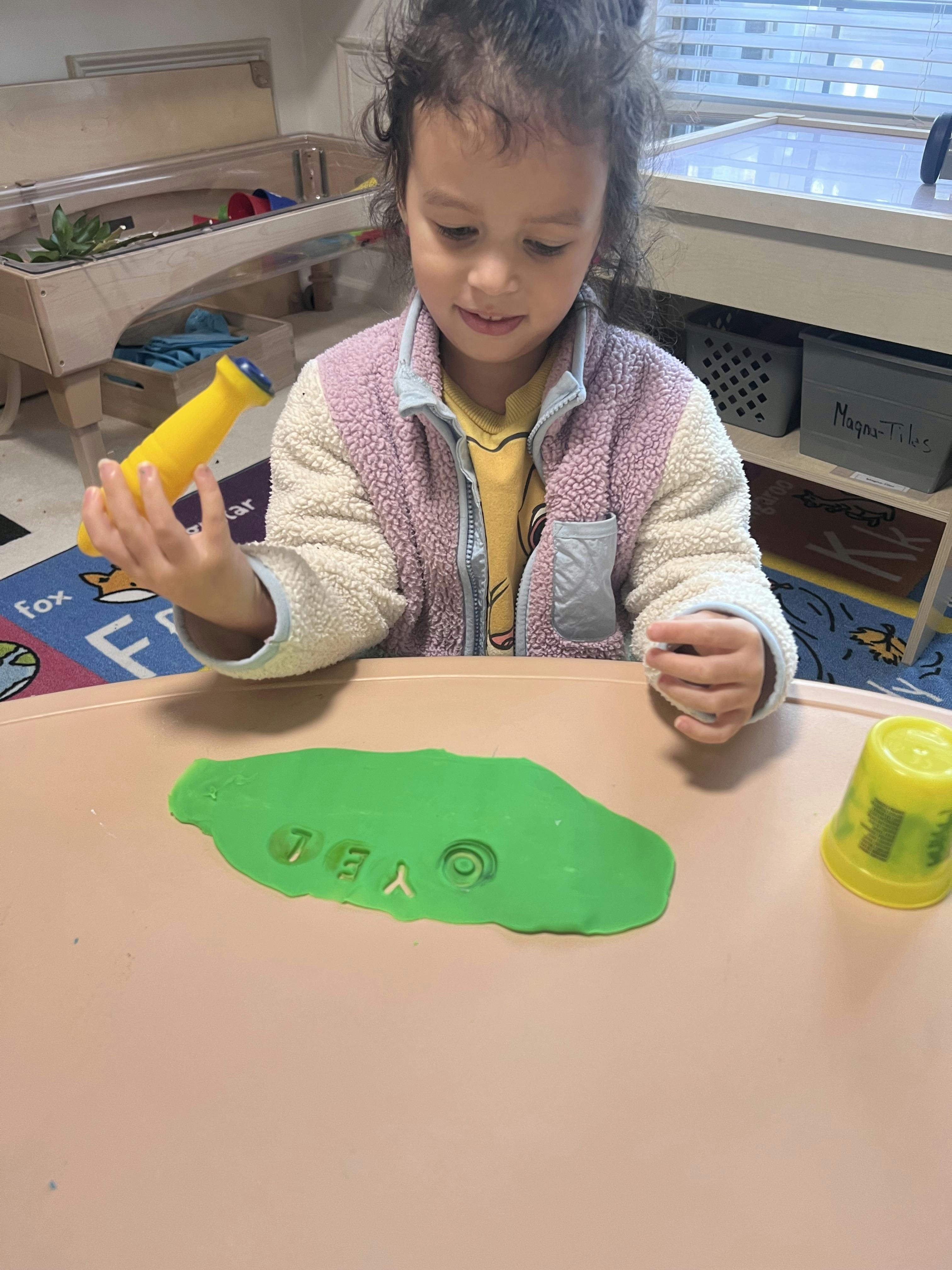 Child playing with green playdough and a yellow toy