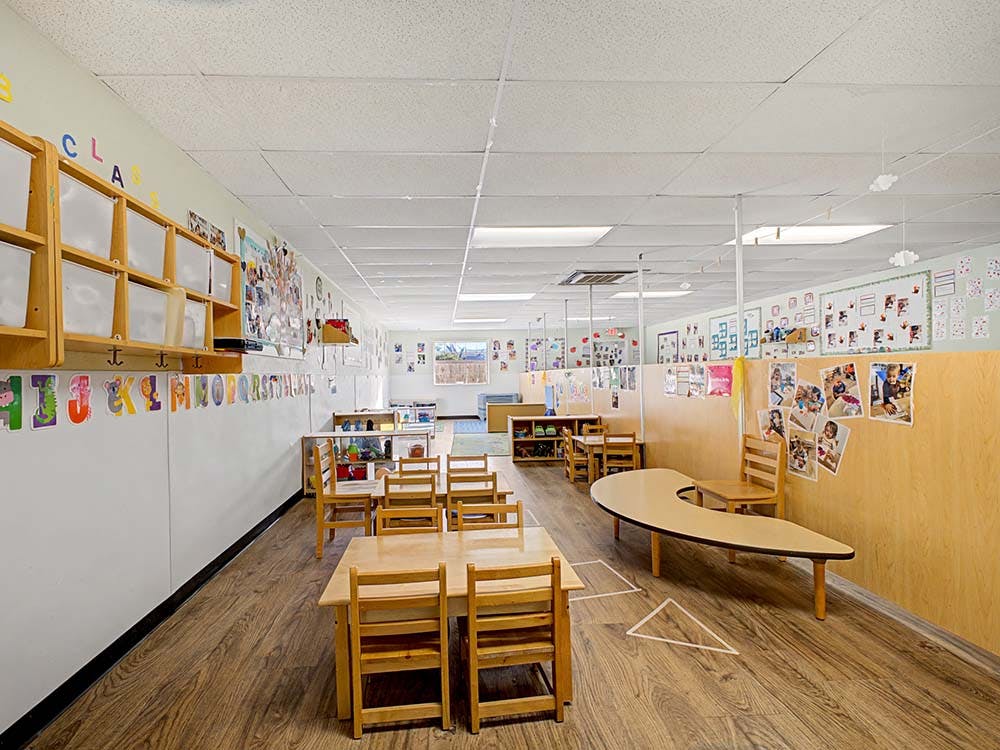 Empty classroom with small wooden tables and chairs, and alphabet decorations on walls