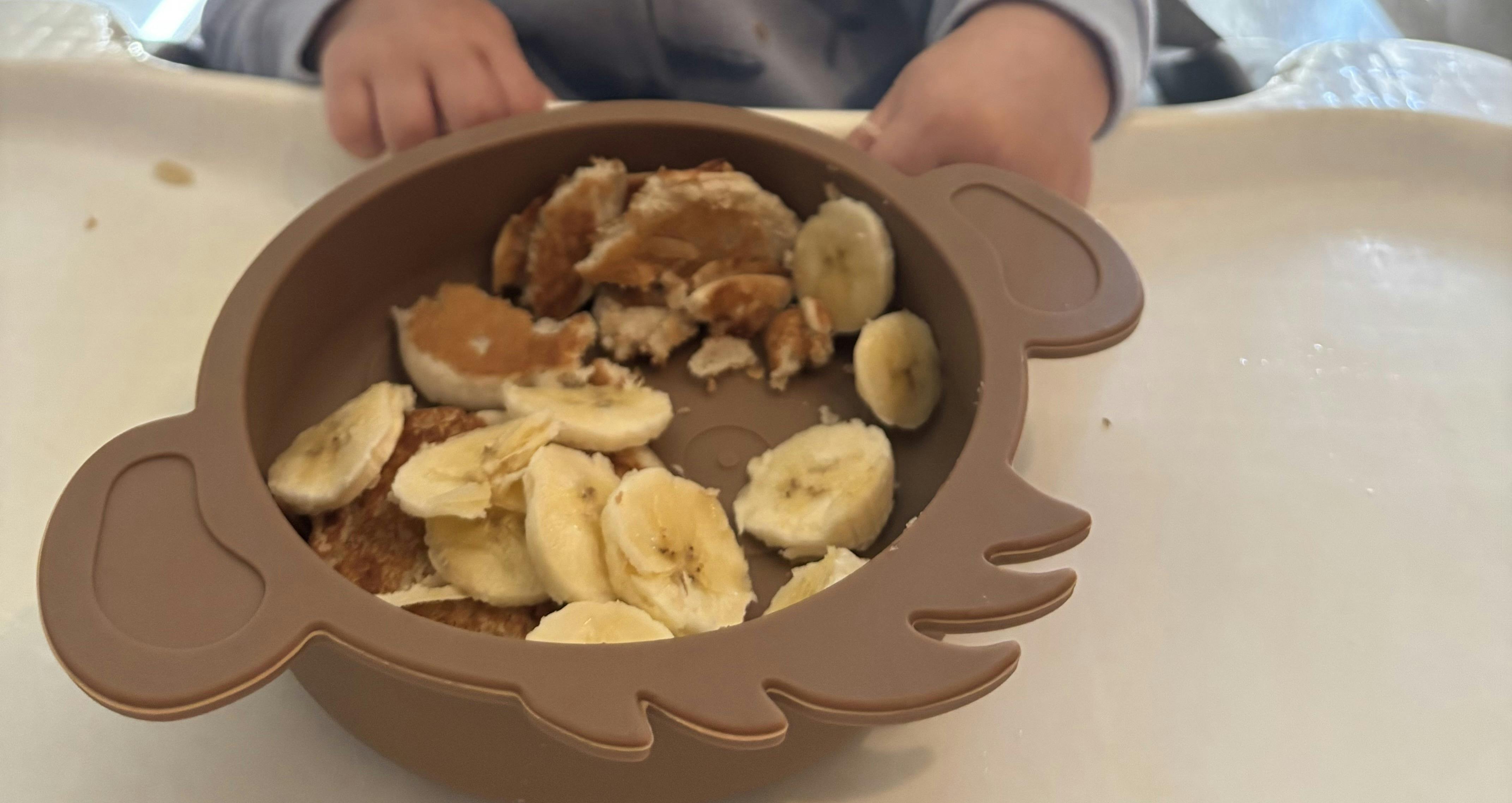 Child's hands near a bowl of sliced bananas and other food