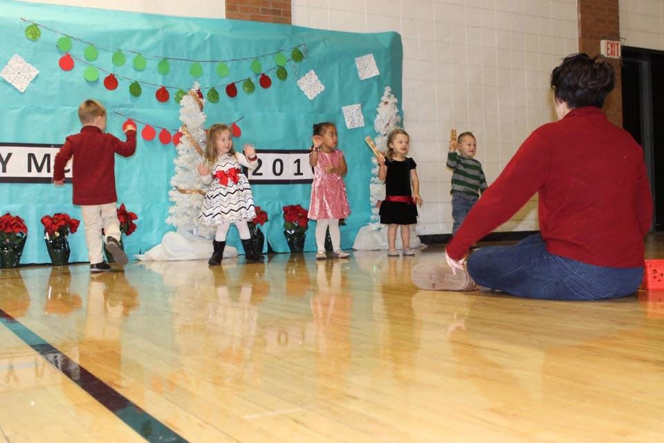 Adult sitting on floor watching children on stage