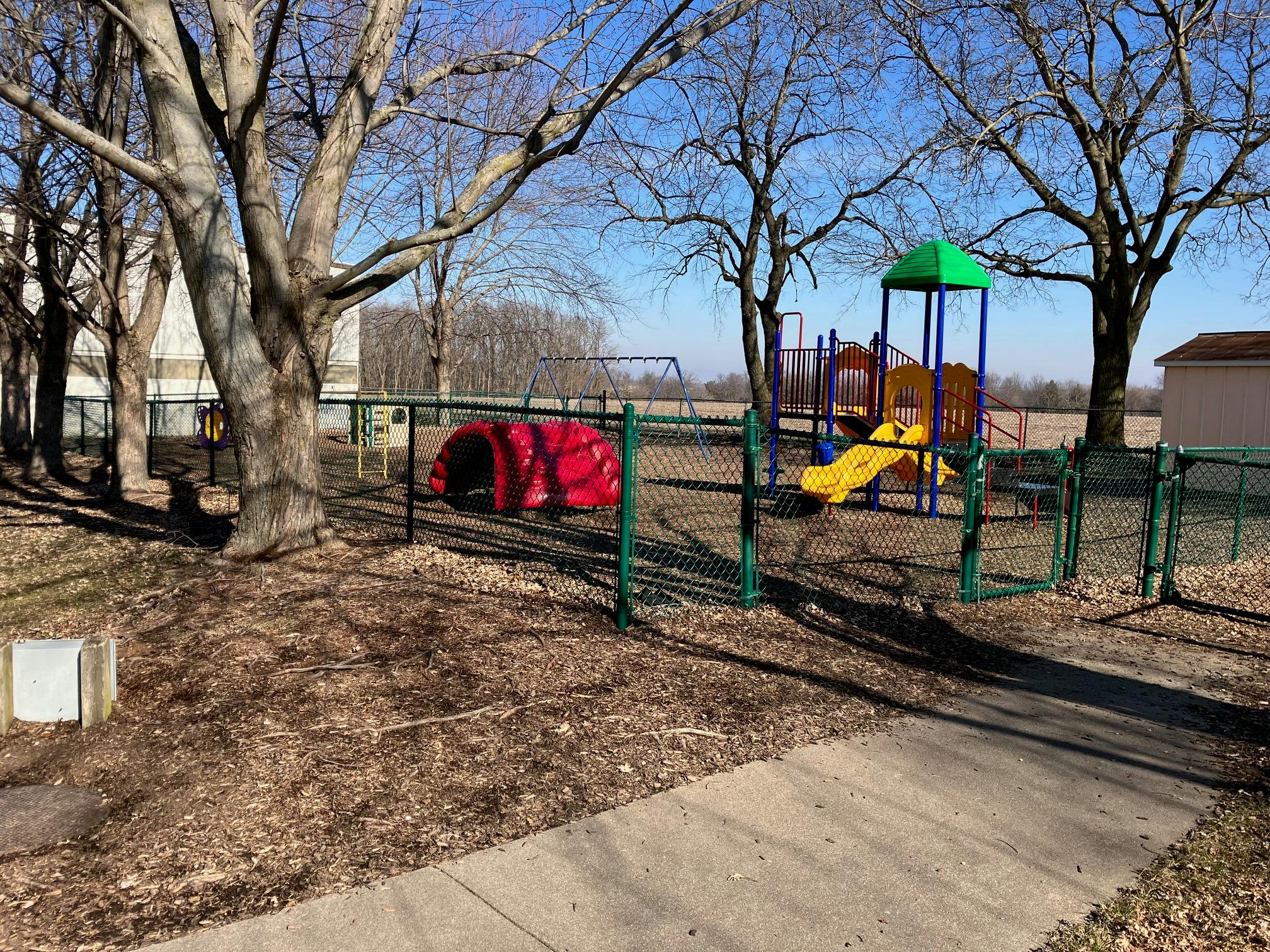Playground with yellow slide and red tunnel behind a chain link fence