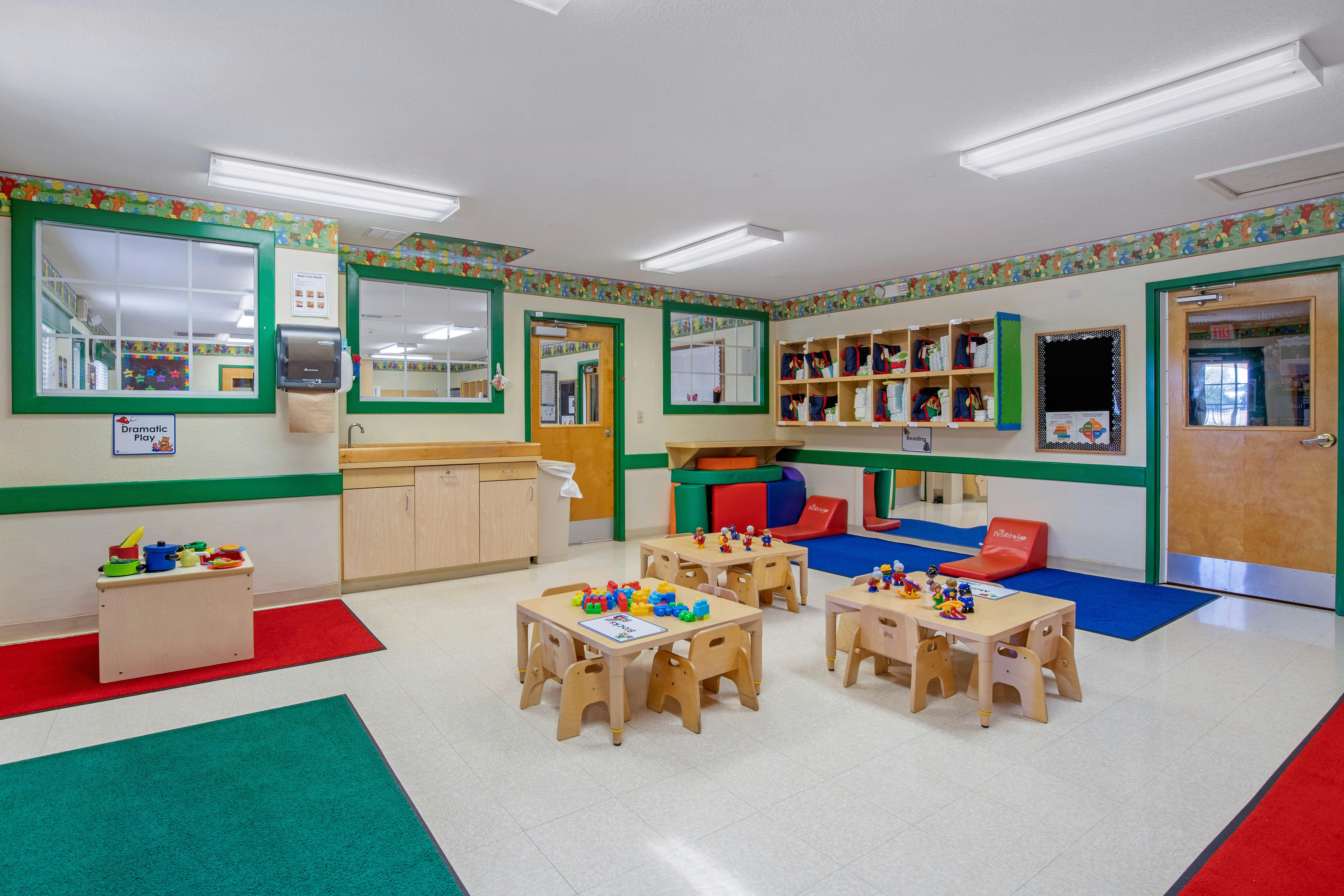 Classroom with small tables and chairs, play kitchen, and storage cubbies