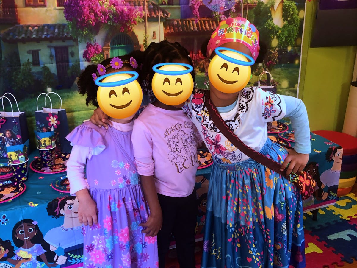 Three children posing in front of a colorful backdrop at a party
