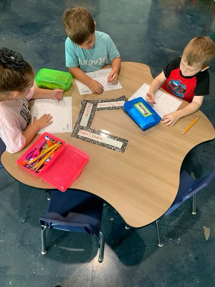 Three children writing at a table in a classroom