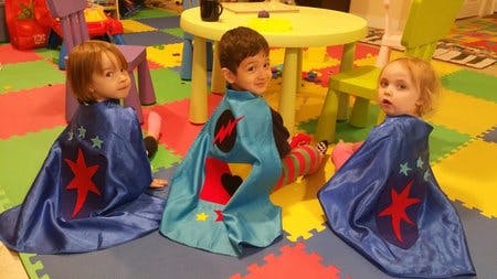 Three children wearing capes sitting on a colorful mat