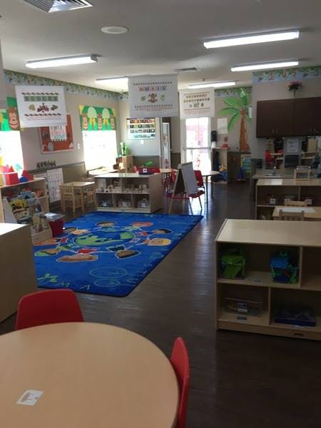 Classroom with a blue rug, small tables, and shelves with learning materials